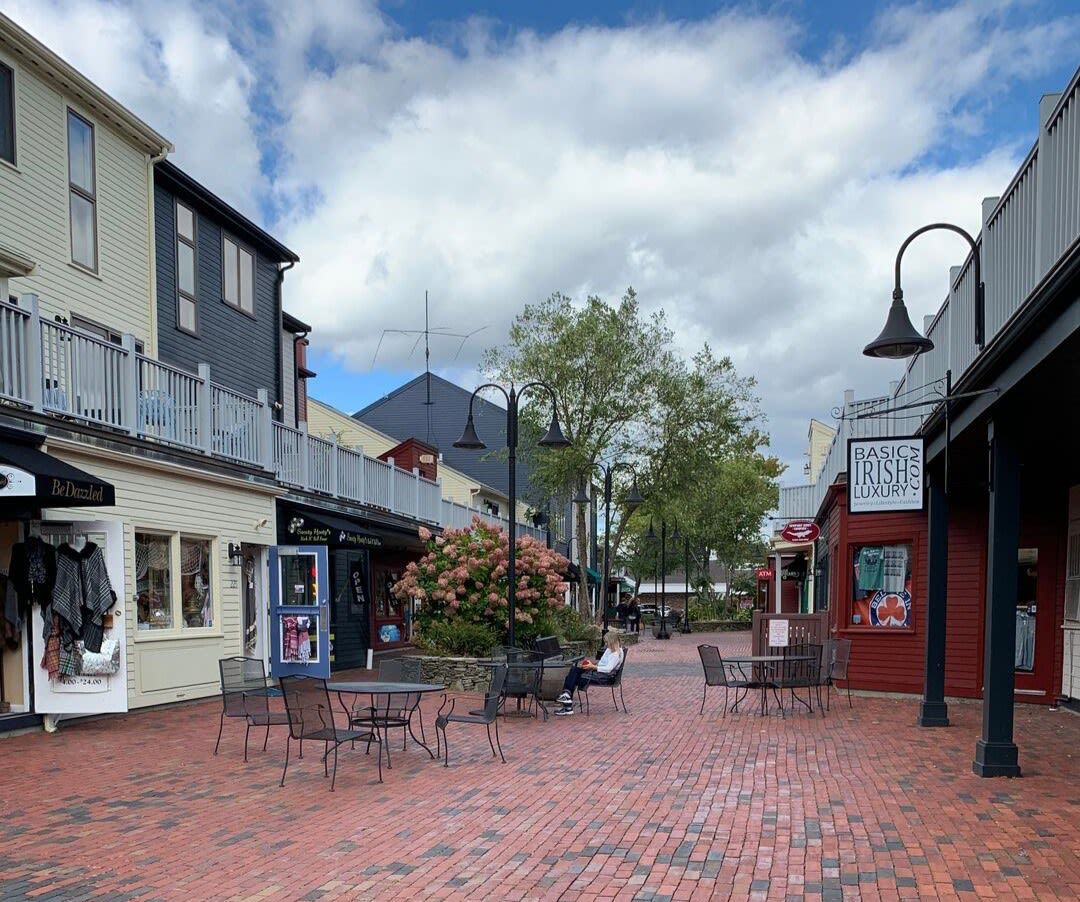 A brick walkway between two buildings with tables and chairs.