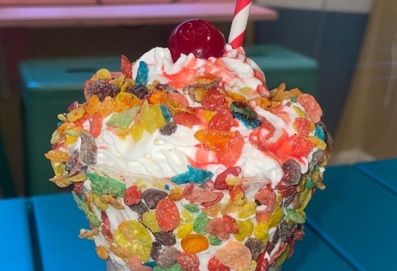 A milkshake with cereal and whipped cream and a cherry on top.