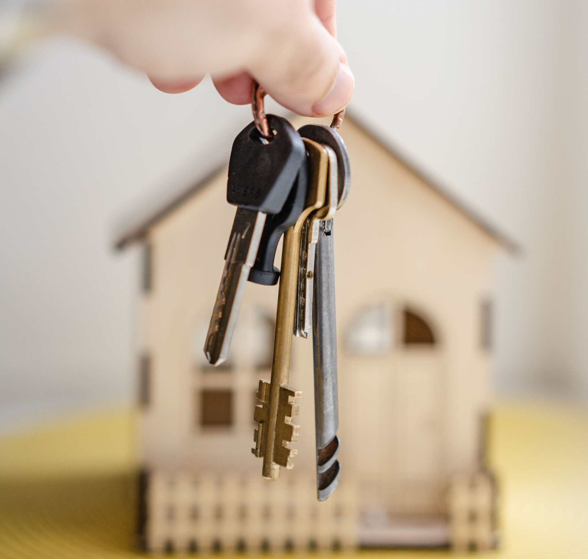A person is holding a bunch of keys in front of a model house.