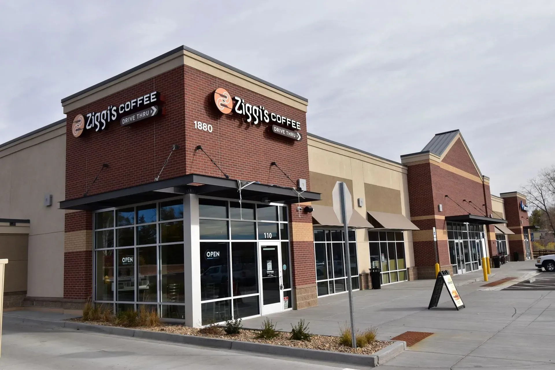Ziggi's Coffee shop exterior. Brick and tan building with large windows and signage, under a cloudy sky.