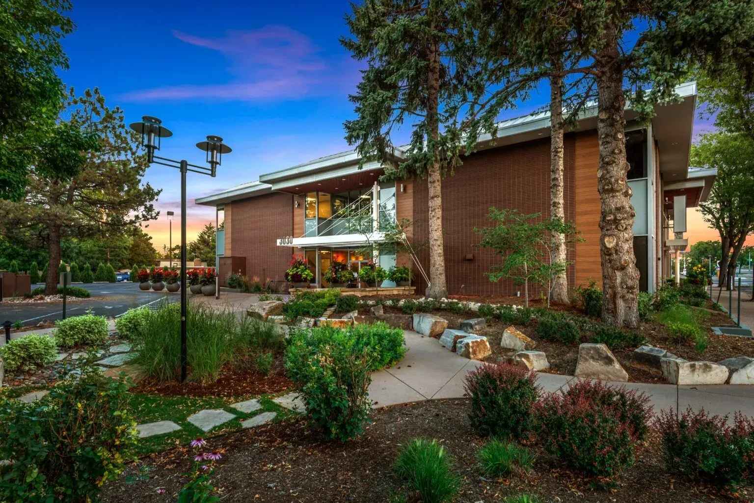 Brick building with landscaped yard and pathway under a blue dusk sky.