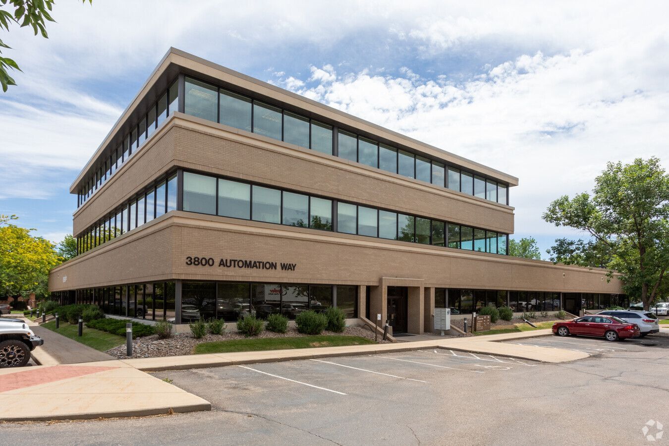 Four-story tan office building with large windows and a parking lot.