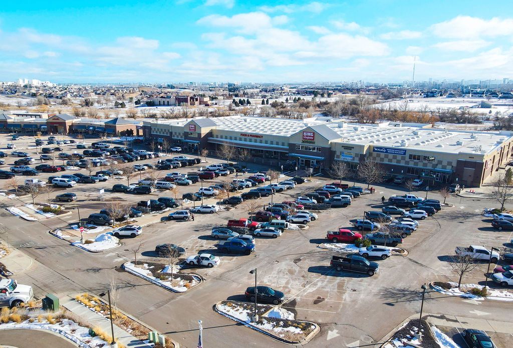 Aerial view of a grocery store with a packed parking lot on a sunny day. Snowy patches present.