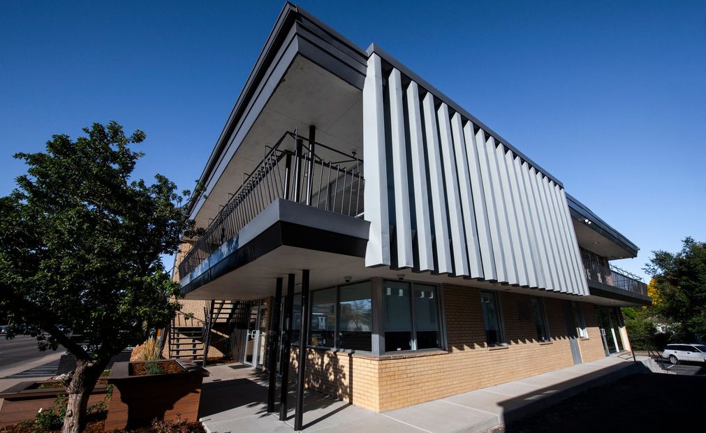 Modern two-story building with vertical gray slats. Balcony with black railing. Sunny, blue sky.