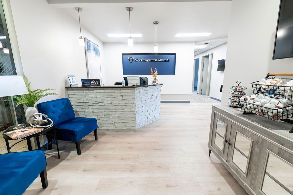 Reception area of a modern office. Blue seating, light wood flooring, a reception desk, and decorative display.