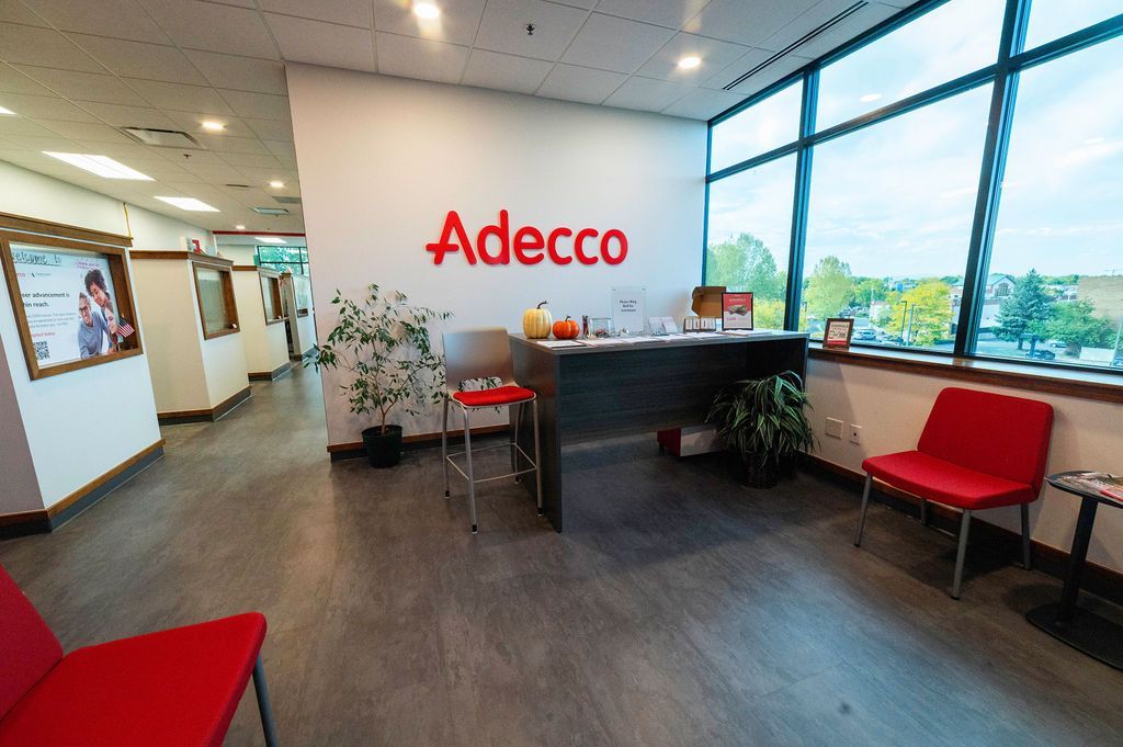 Adecco office reception area with red chairs, logo on the wall, and a large window with an outdoor view.