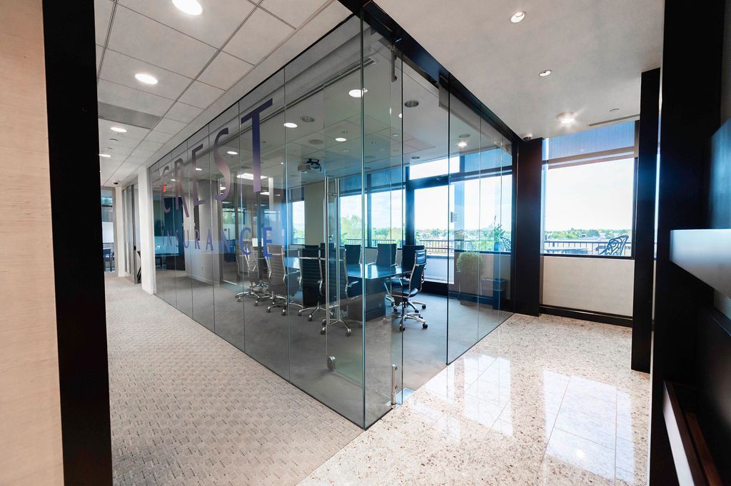 Glass-walled office space with conference room visible through the glass. Bright natural light and speckled flooring.