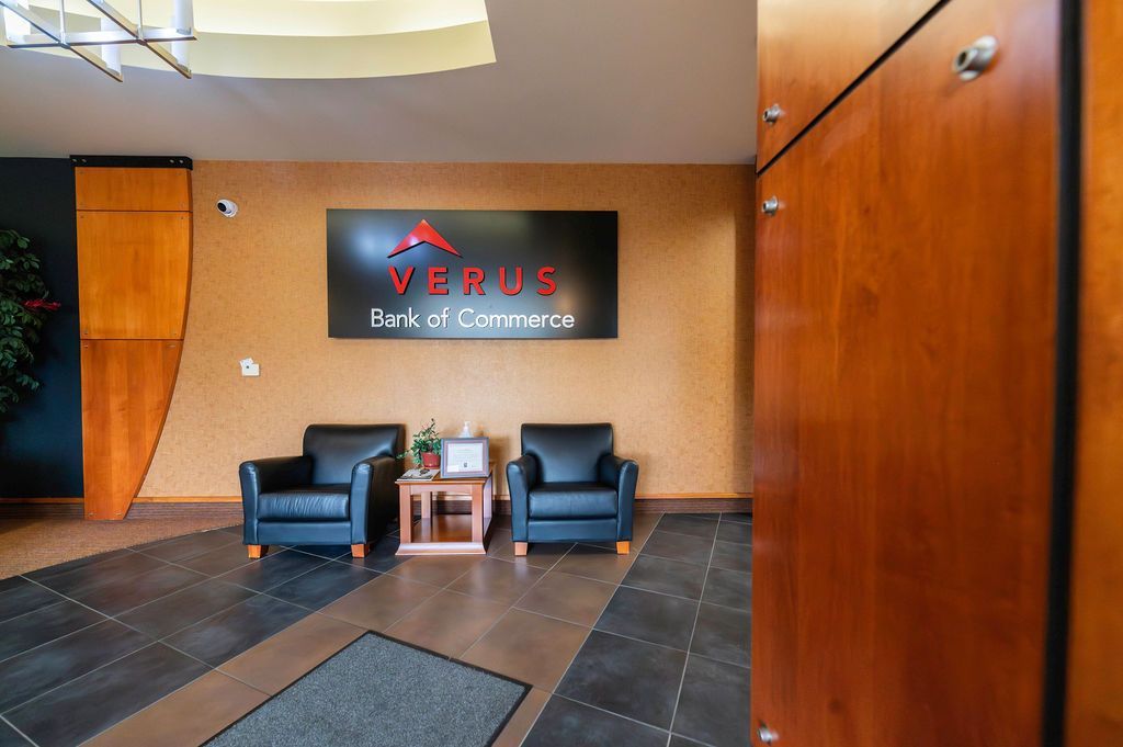 Lobby with black leather chairs, wood paneling, a sign for Verus Bank & Commerce.