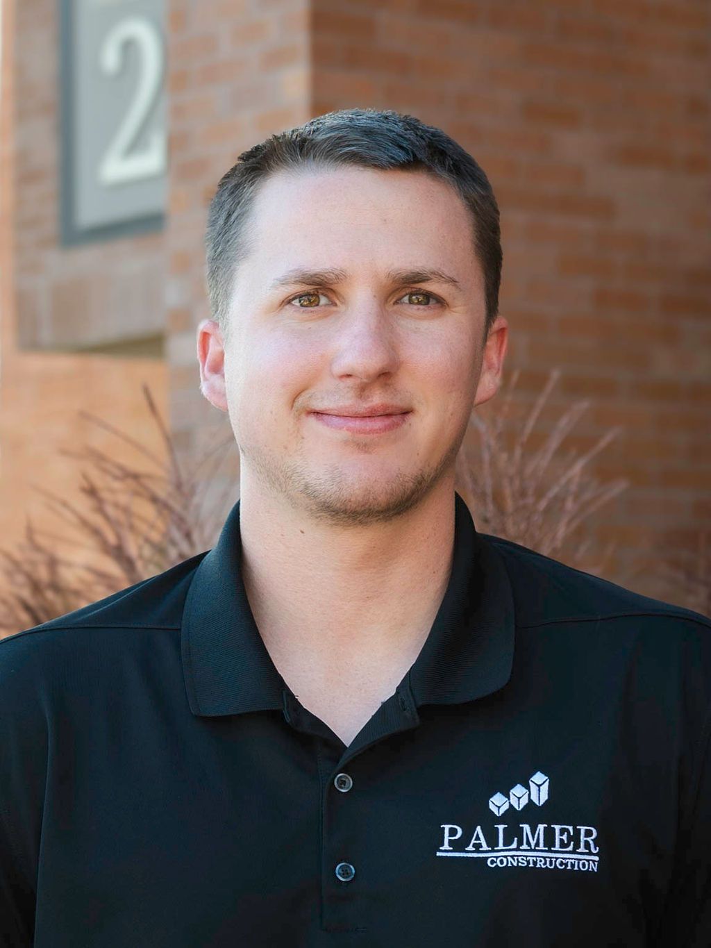 Man in black polo shirt smiles outdoors, Palmer Electric logo visible.