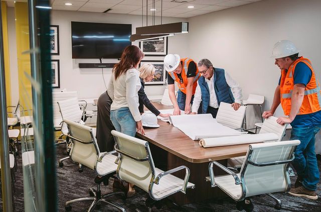Construction team reviewing blueprints around a conference table in an office.