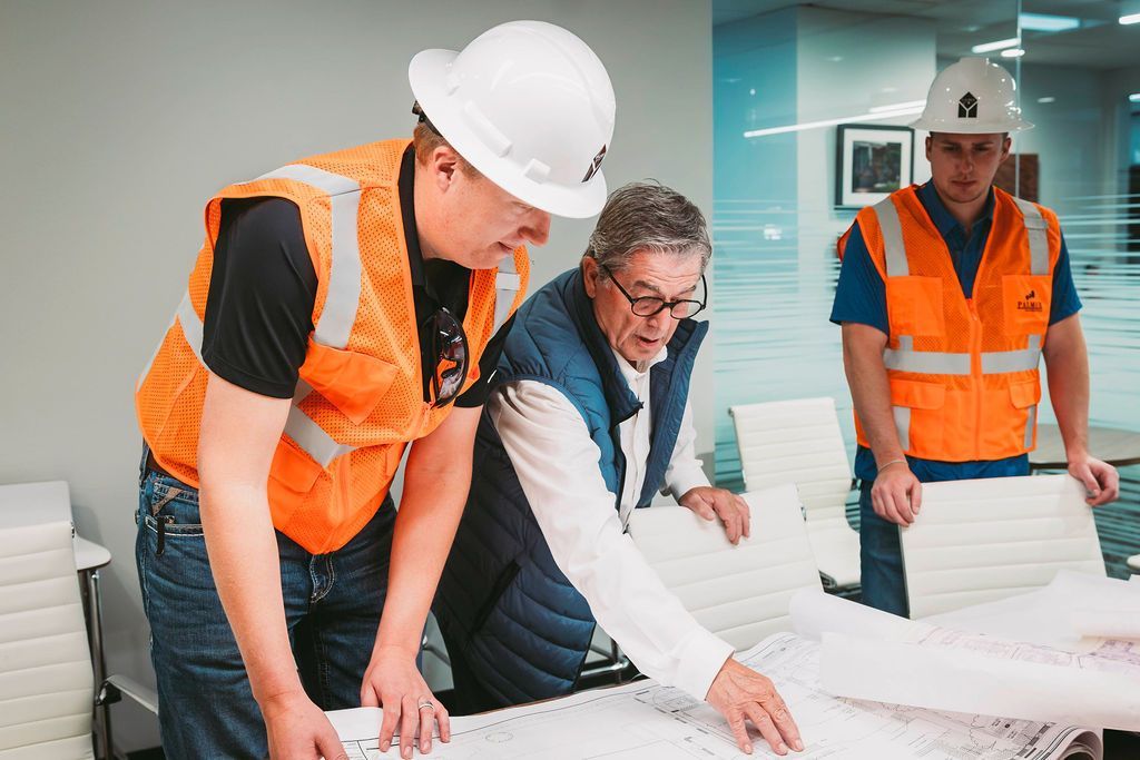 Photo of construction team looking at blueprints and wearing hard hats and vests