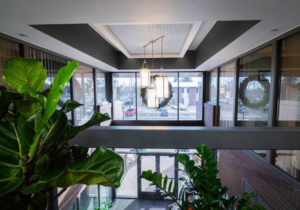 Interior view of a building lobby with large windows and a hanging light fixture. Plants are in the foreground.