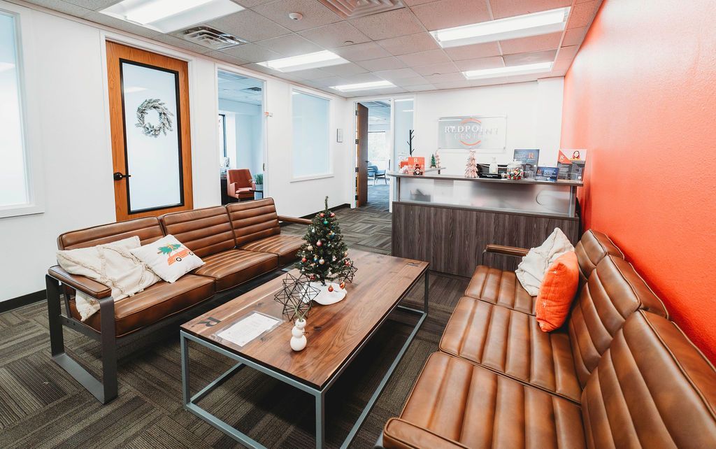 Office waiting area with brown leather couches, a coffee table, and an orange accent wall.