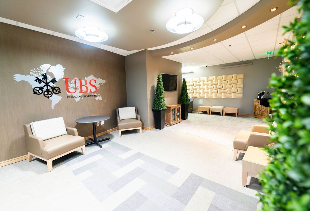 UBS office waiting area with seating, logo, and decorative plants. Beige, gray, and brown color scheme.