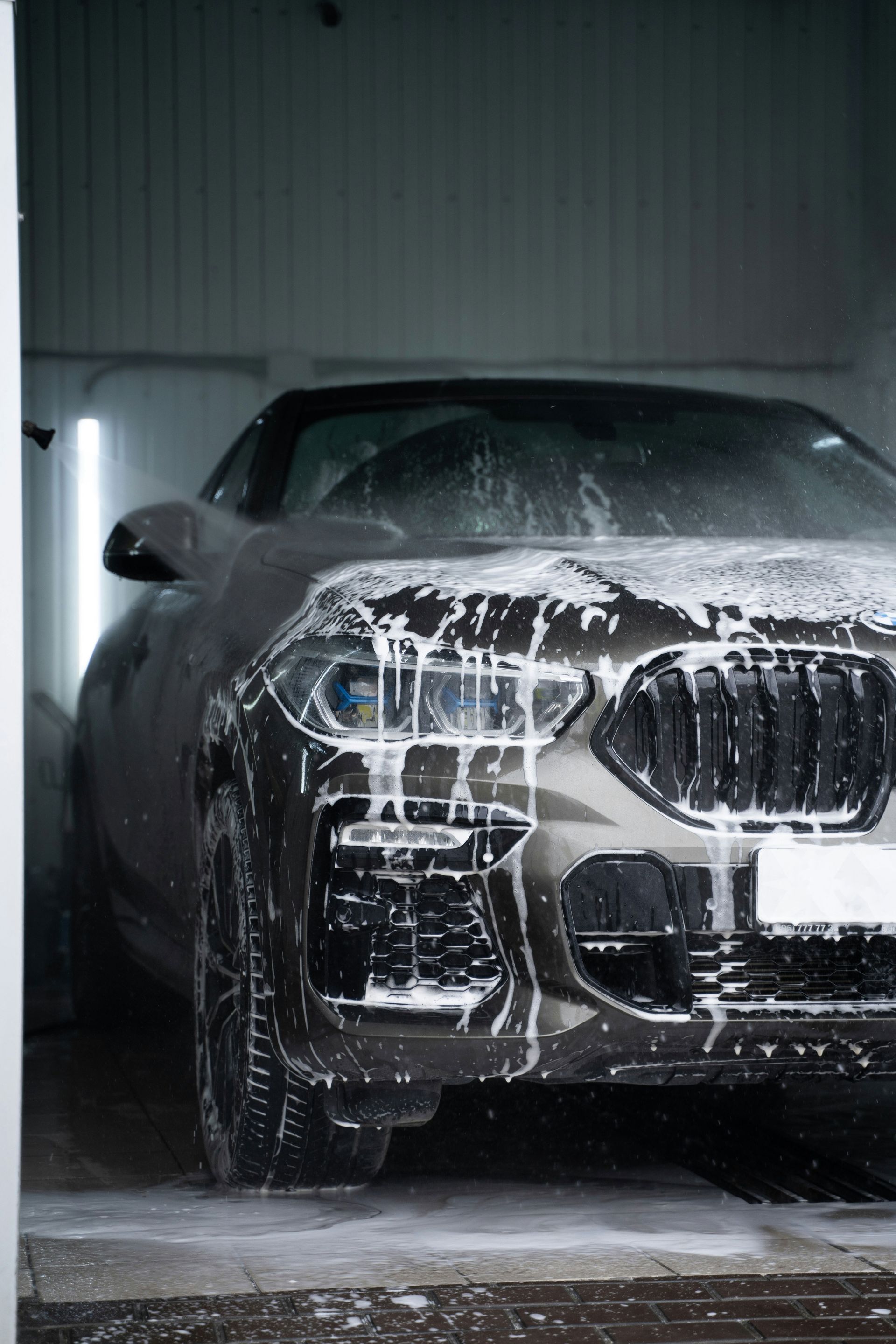 Black SUV covered in foam during a car wash in a dim indoor bay