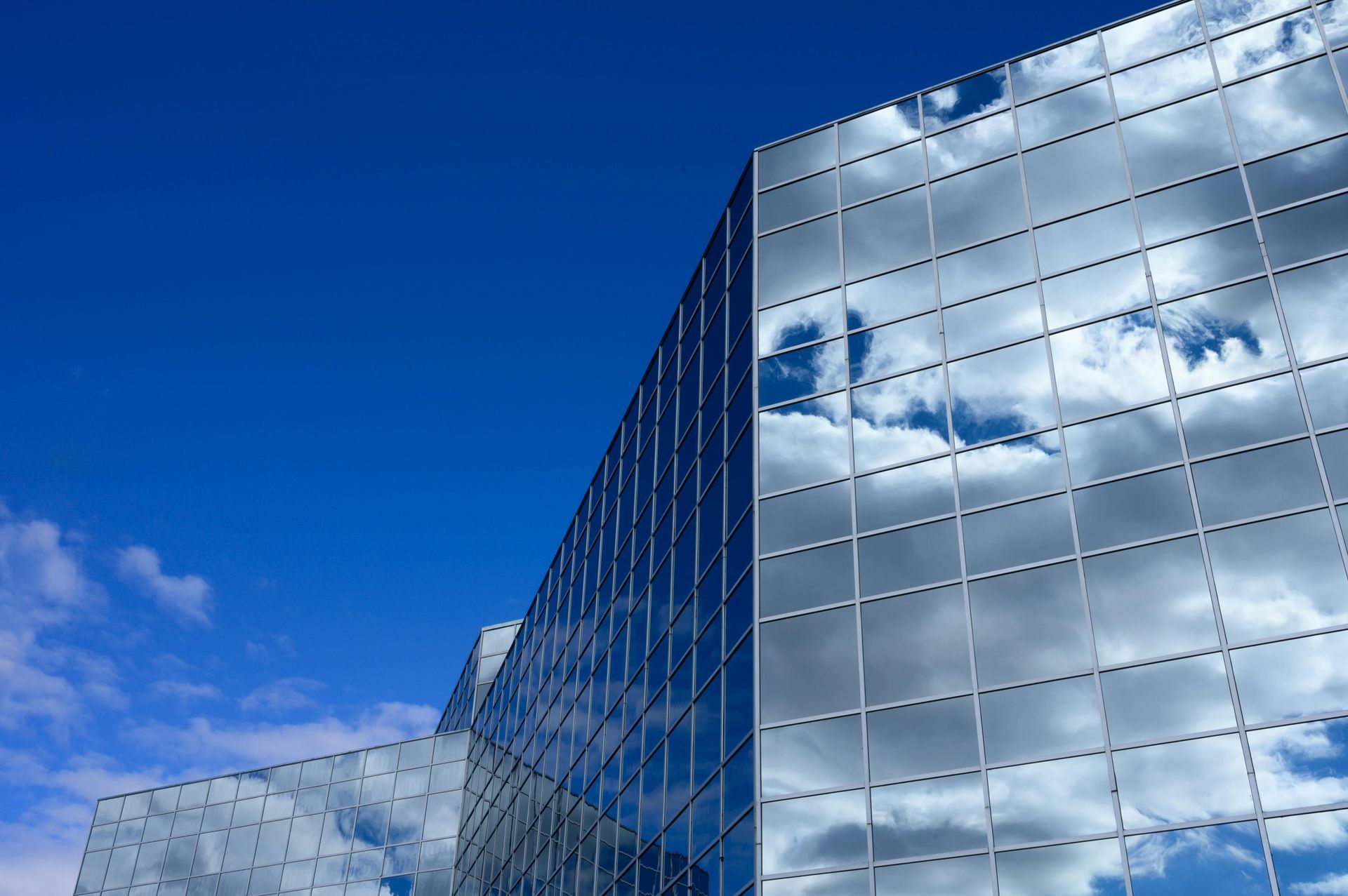 Modern glass office building reflecting clouds under a bright blue sky