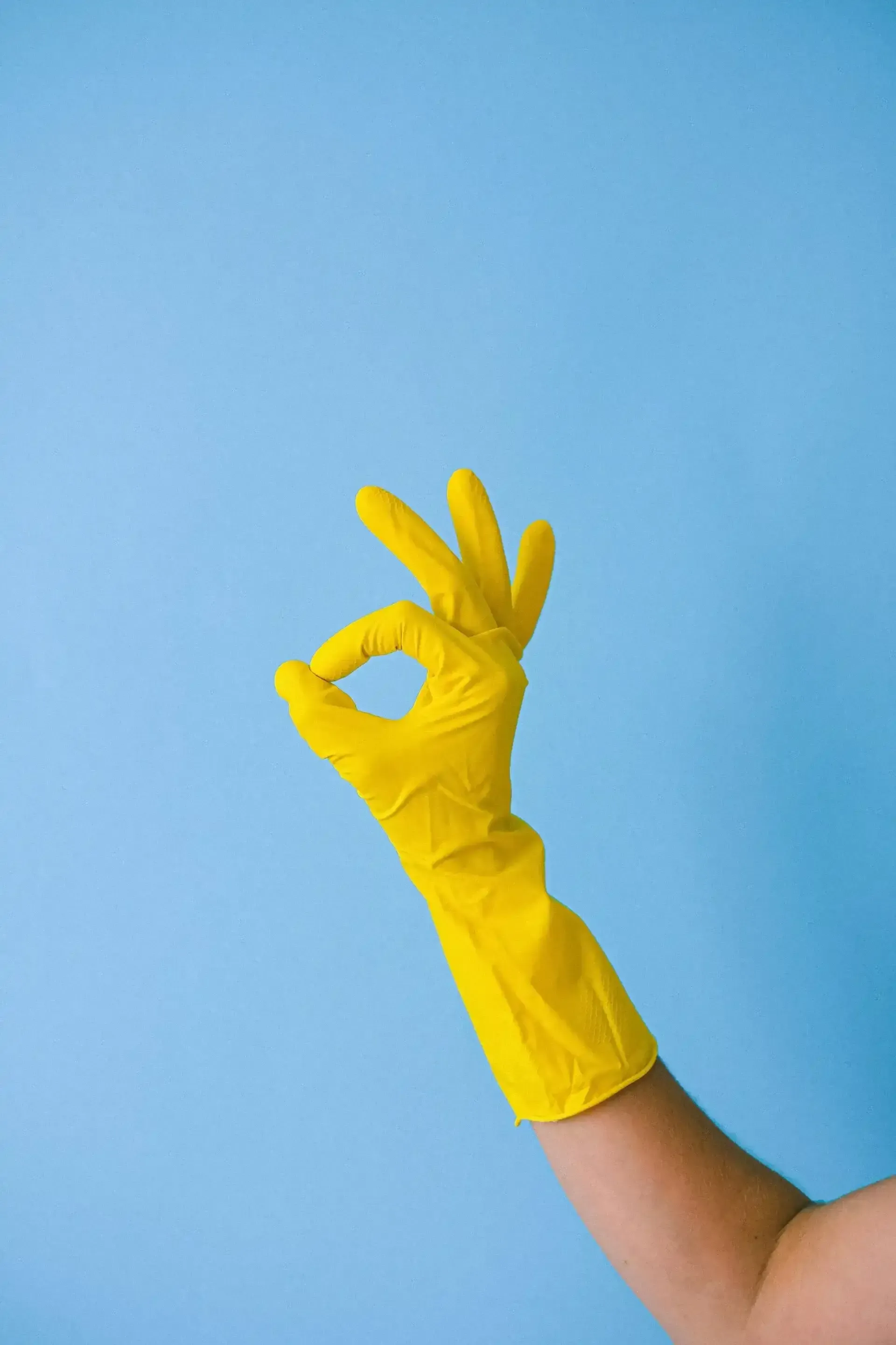 A hand in a yellow rubber glove making an OK sign against a blue background