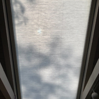 A rectangular skylight covered by a translucent pleated shade, with silhouettes of tree branches cast upon the surface.