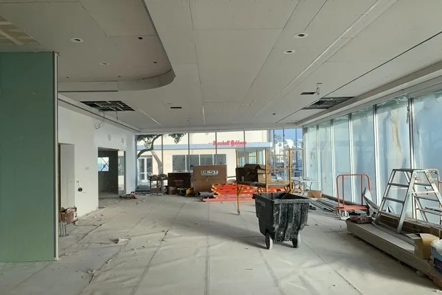 Empty storefront under renovation with debris, ladders, and construction materials on the floor
