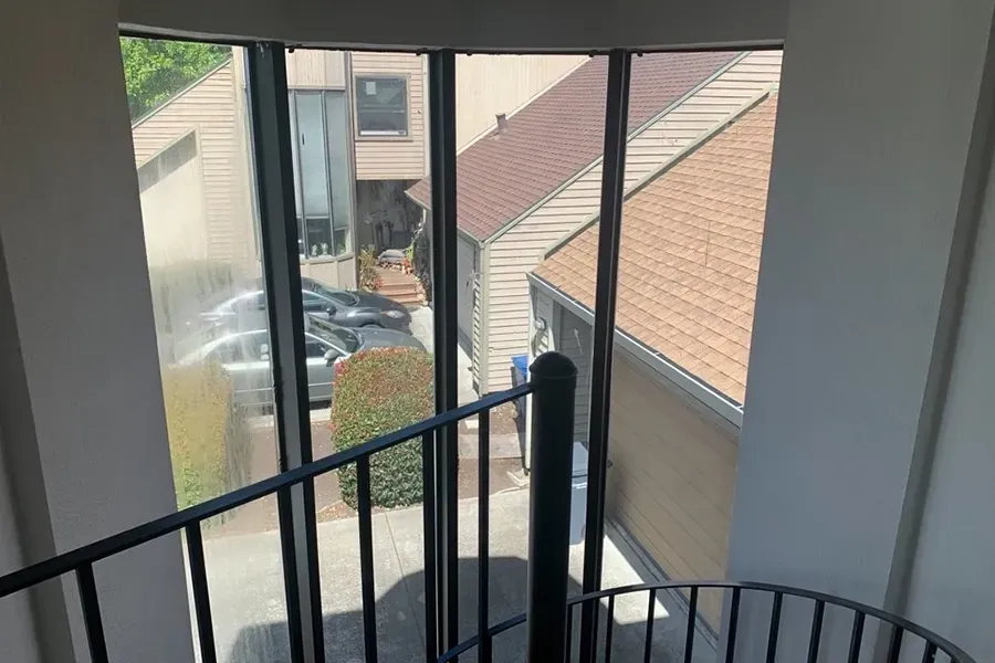View from an apartment balcony overlooking a parking lot and neighboring buildings through curved windows.