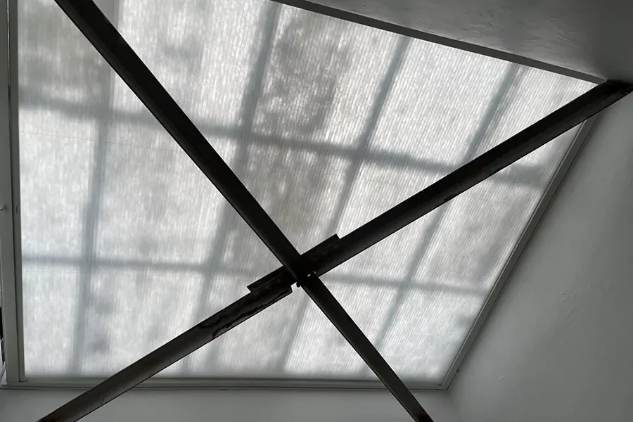 Crossed black metal bars over a sunlit frosted window, casting a grid-like shadow.