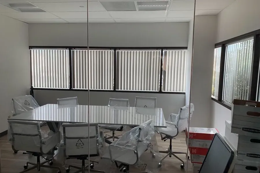 Conference room with a round table, white chairs, and vertical blinds on the windows