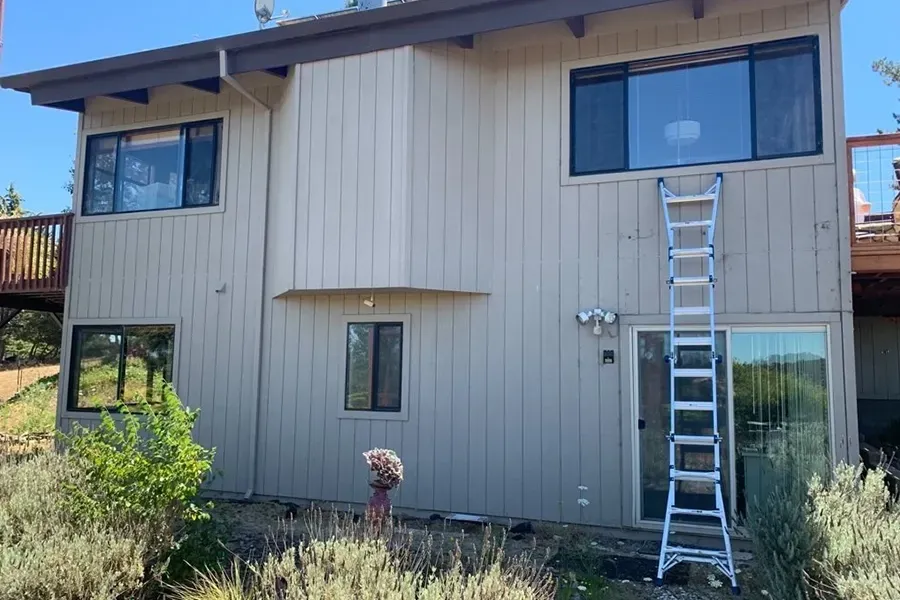 Two-story tan house exterior with a ladder leaning against the upper right side.