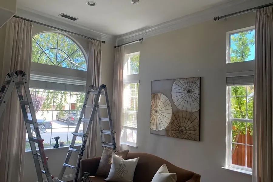 Bright living room with two ladders, large arched window, and wall art above a sofa