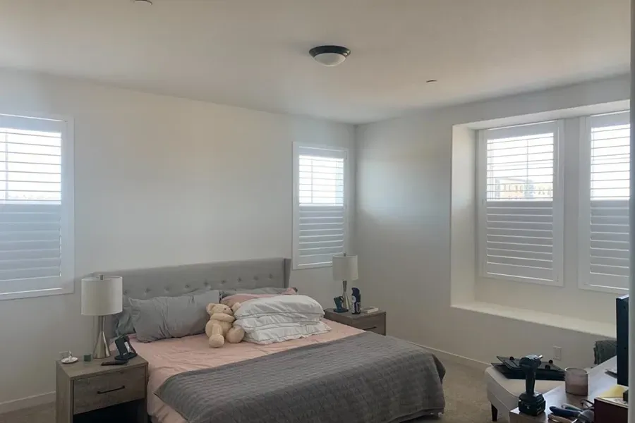 Bright bedroom with a gray bed, white shutters, and a ceiling fan in a neat, minimalist room