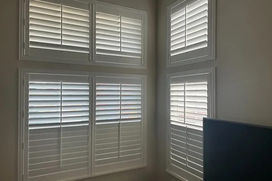 Sunlit corner with white plantation shutters and a partial view of a dark TV screen