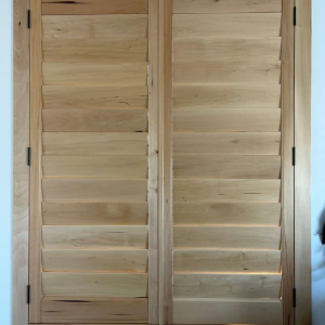 Two wooden interior window shutters with horizontal slats installed in a frame against a white wall.