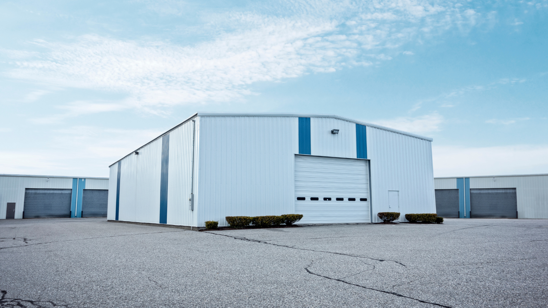 White warehouse with blue trim and garage door, against a blue sky.