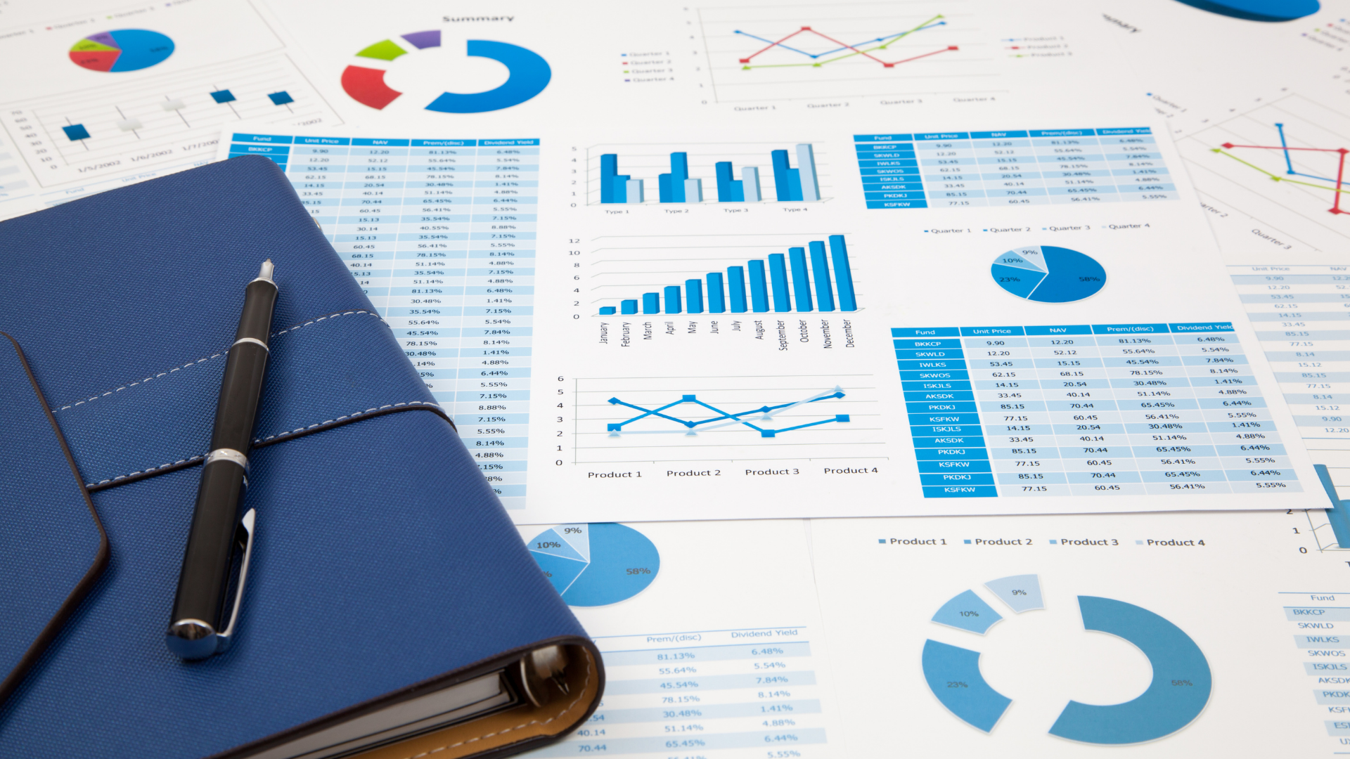 Blue notebook and pen on a desk covered with various charts and graphs 