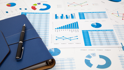 Blue notebook and pen on a desk covered with various charts and graphs