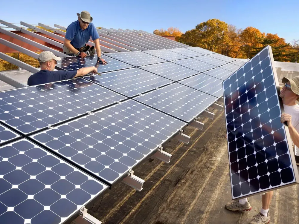 Solar panel installation on a roof with three workers. Blue panels, autumn trees.