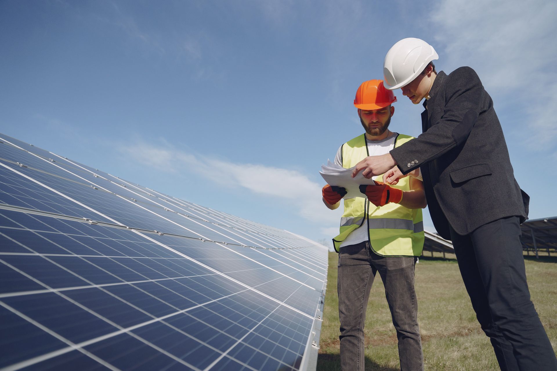Two engineers reviewing plans beside a solar panel array under a blue sky