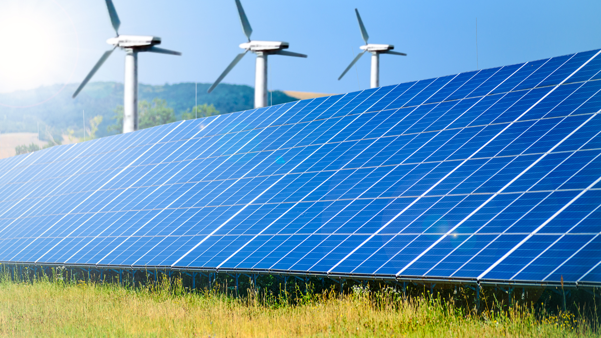Solar panels and wind turbines in a field, representing renewable energy.
