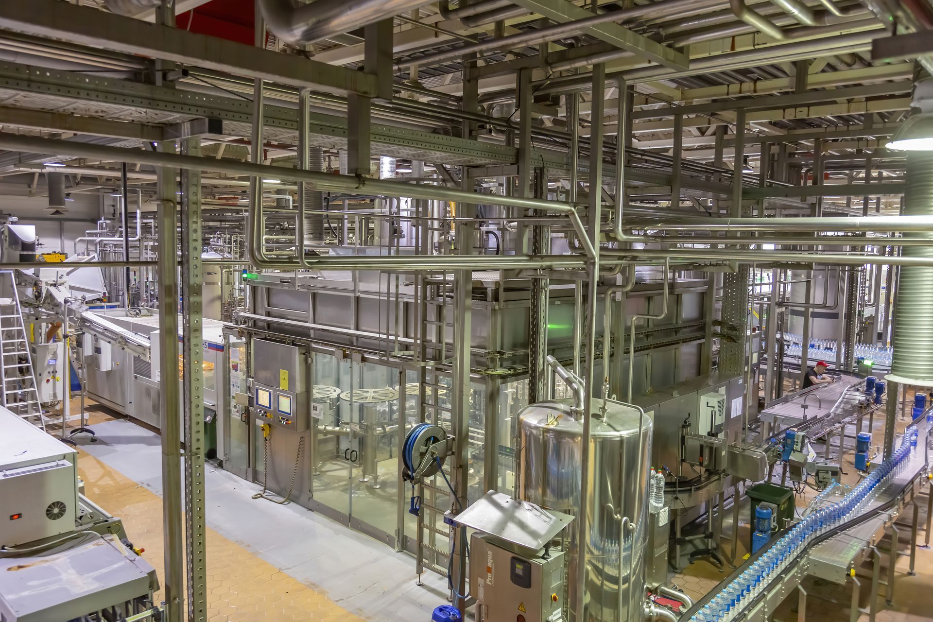 Industrial interior of a factory with stainless steel pipes, machinery, and conveyor belts.