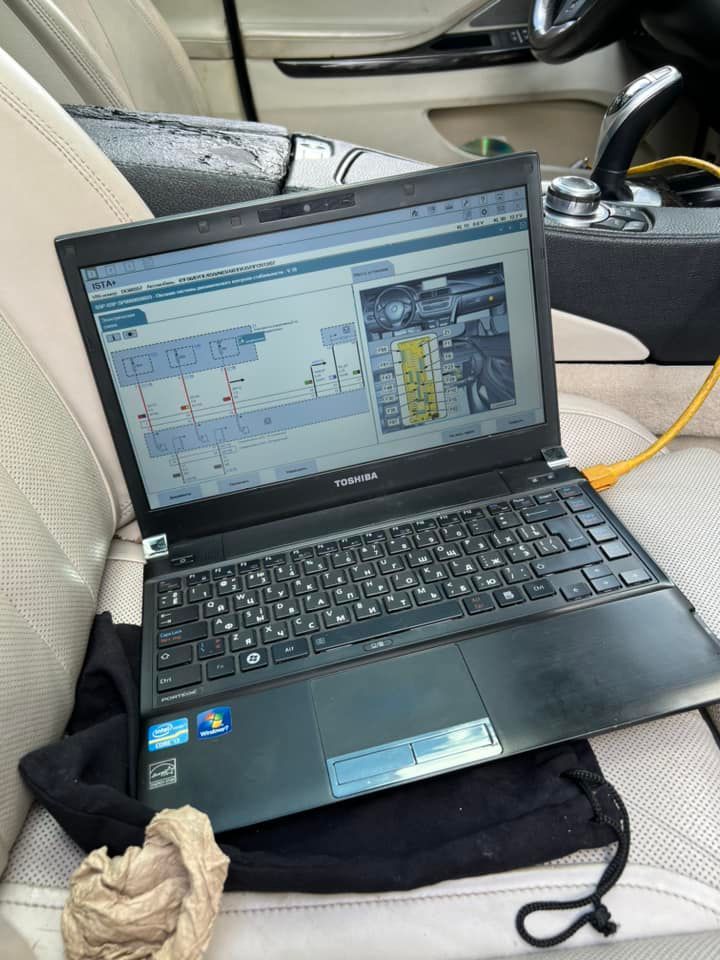 Laptop on a car seat displaying a technical diagram, with a yellow cable plugged in nearby.