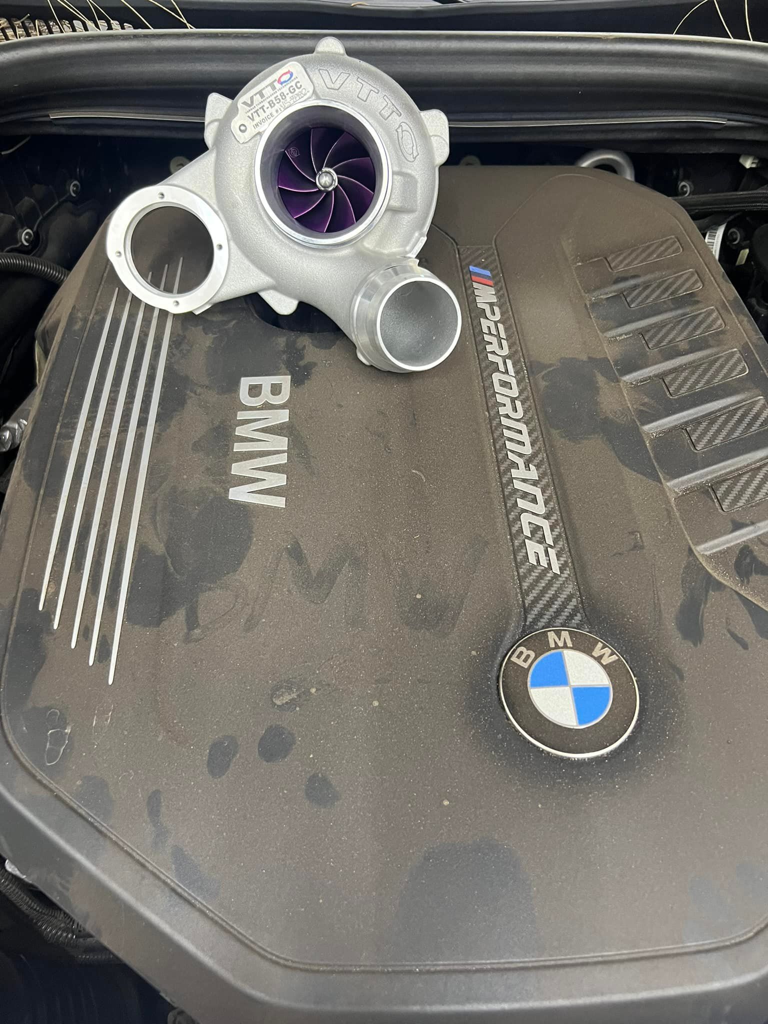 Silver turbocharger resting on a dusty BMW engine cover with the BMW logo visible.