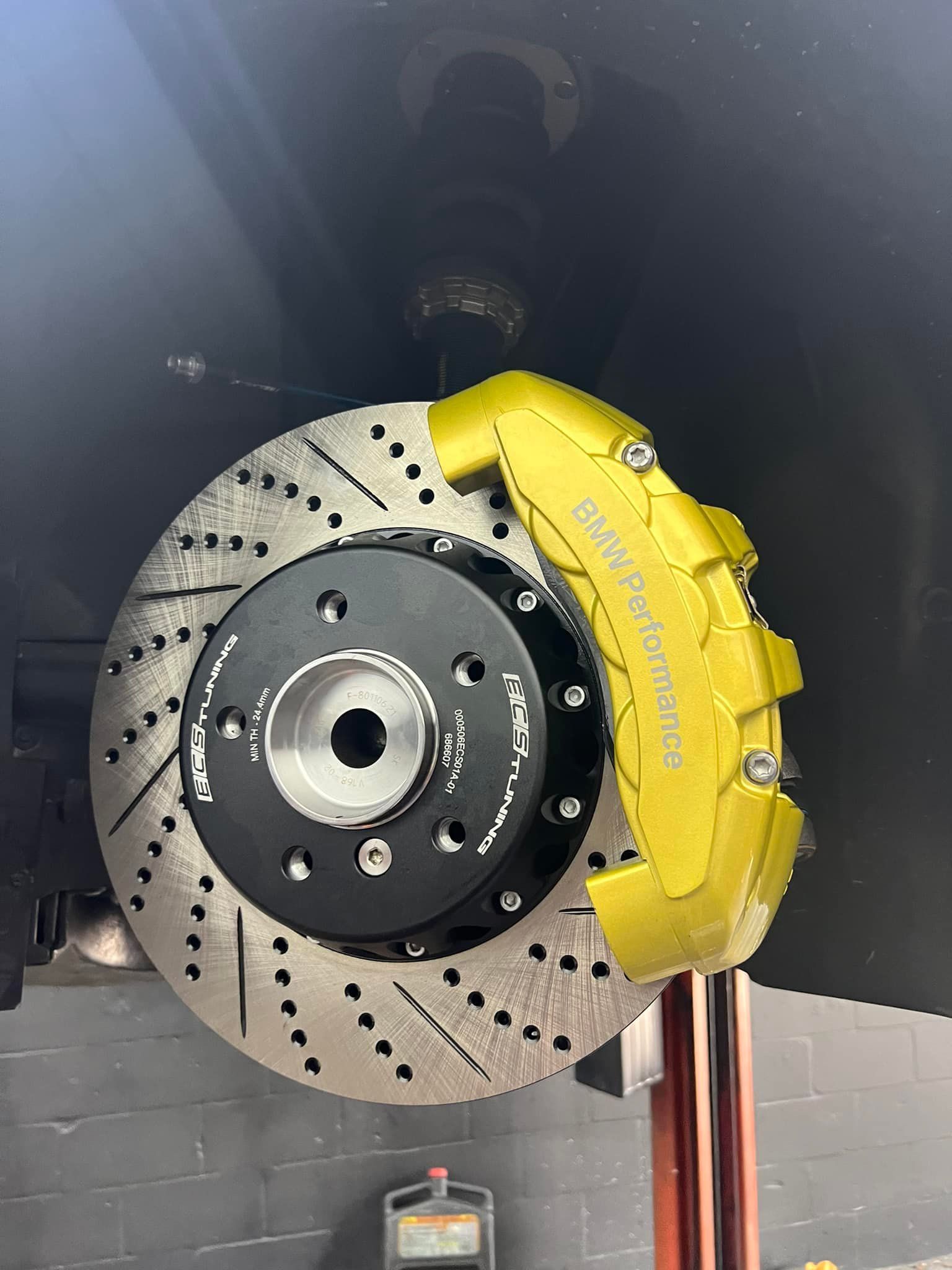 Close-up of a yellow brake caliper and drilled disc brake assembly on a vehicle.