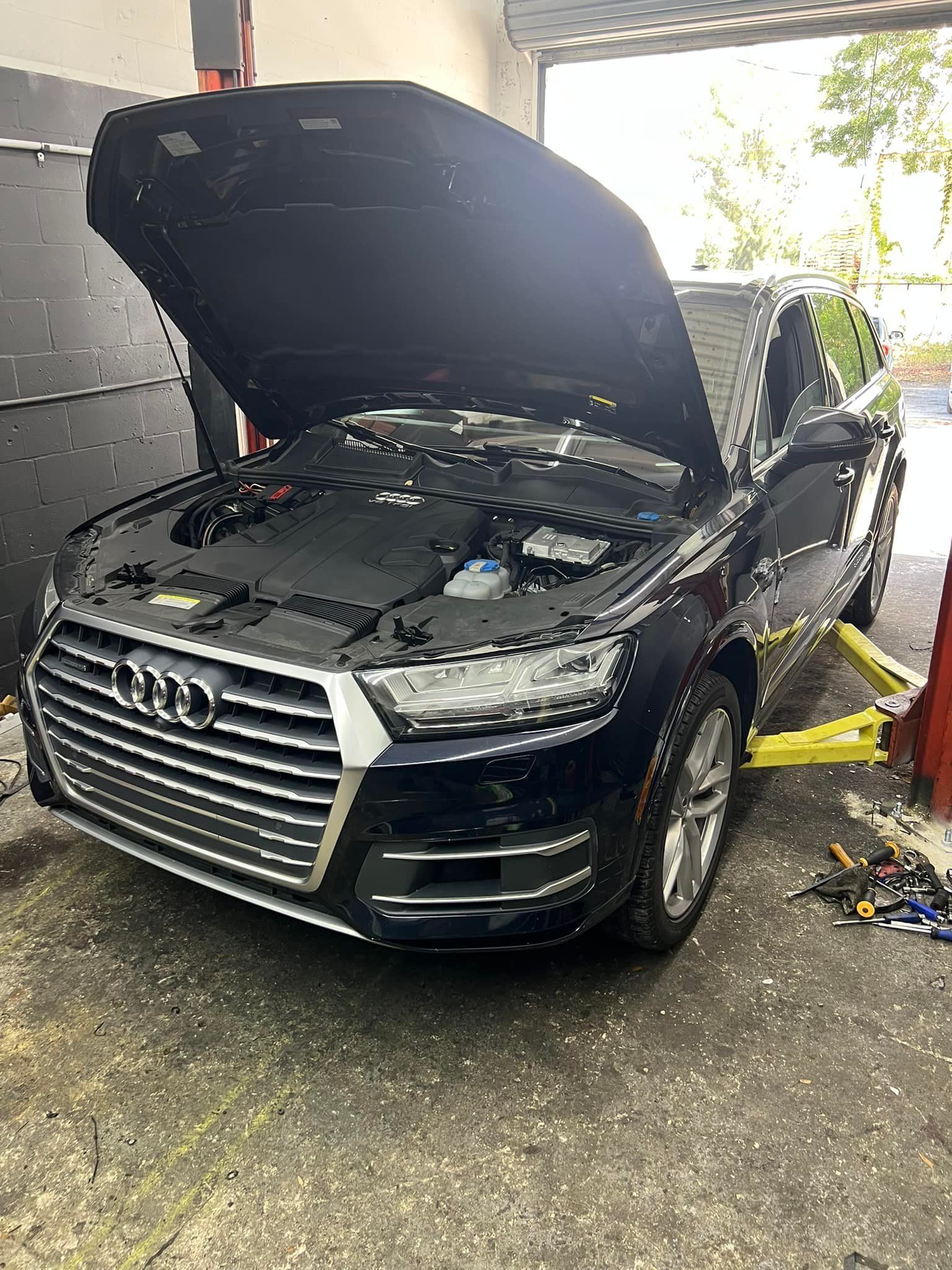 Black Audi SUV with hood open in a driveway, front bumper damaged, near a garage.