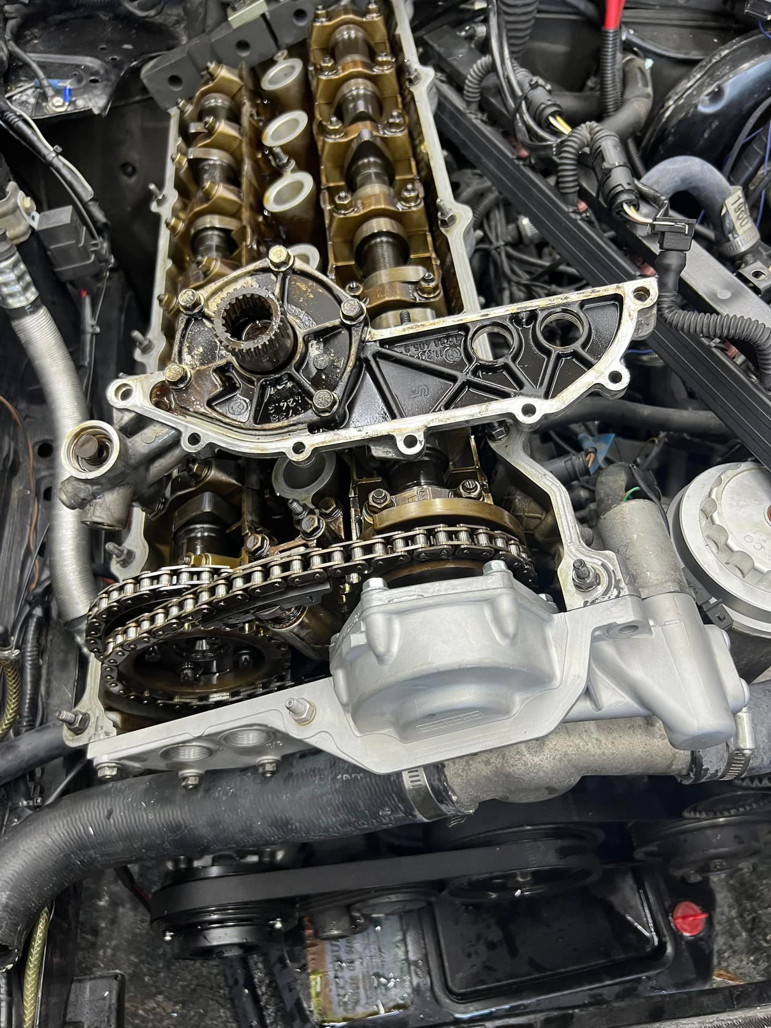 Car engine with the valve cover removed, exposing camshafts, timing chain, and engine components.