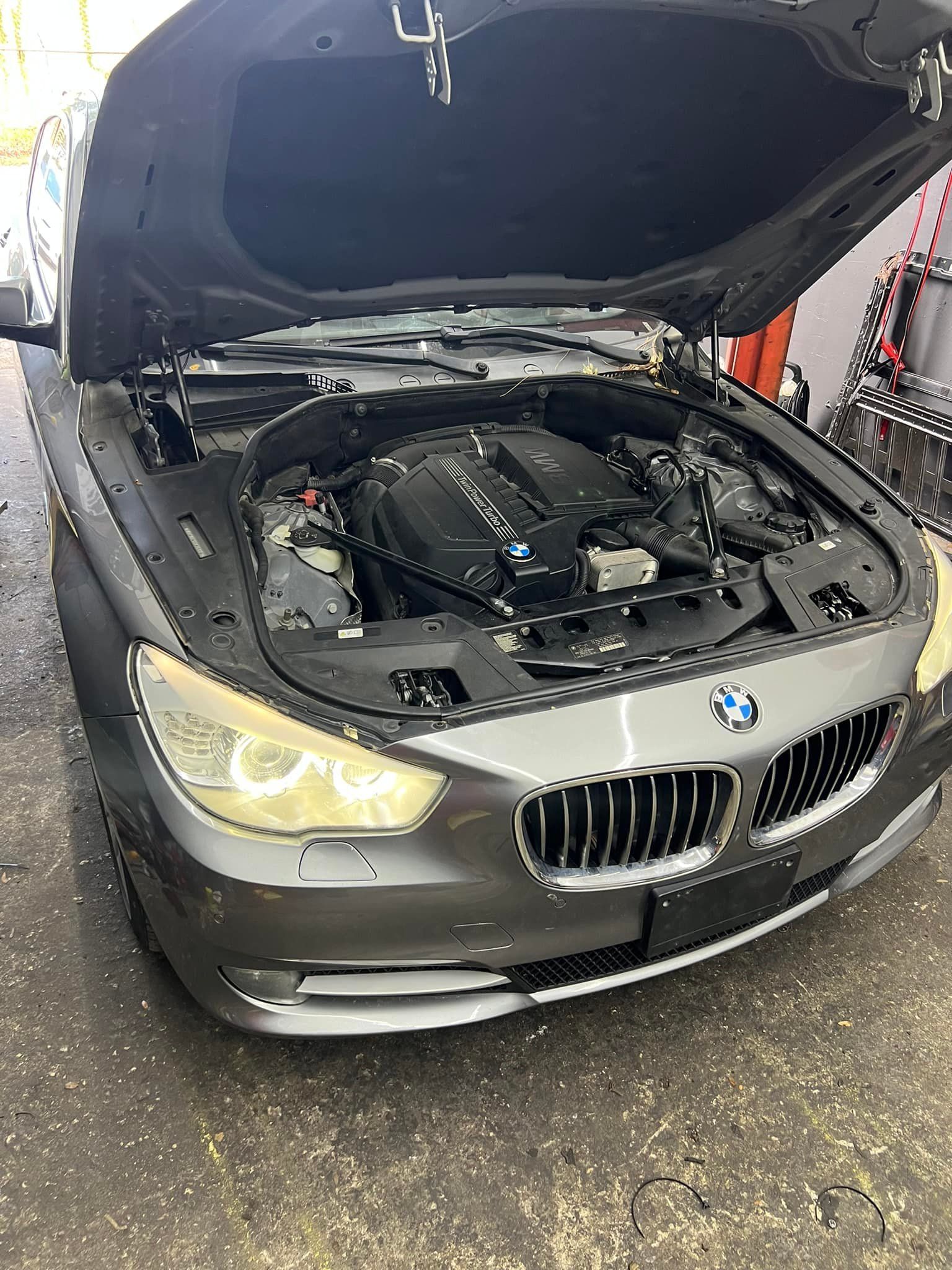 BMW sedan with hood open, showing the engine in a garage.