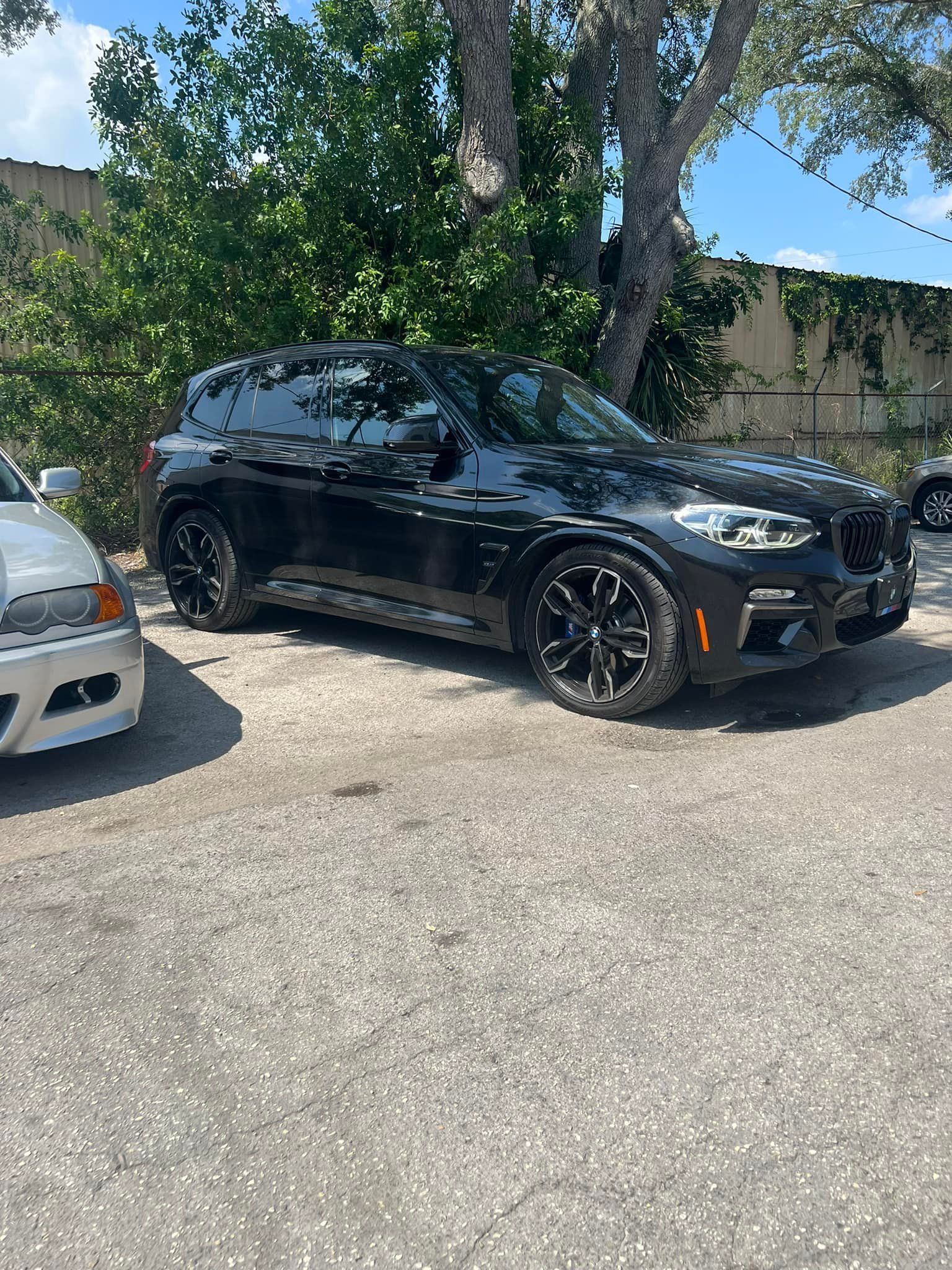 Black SUV parked in a lot beside a white car, with trees and a building in the background.
