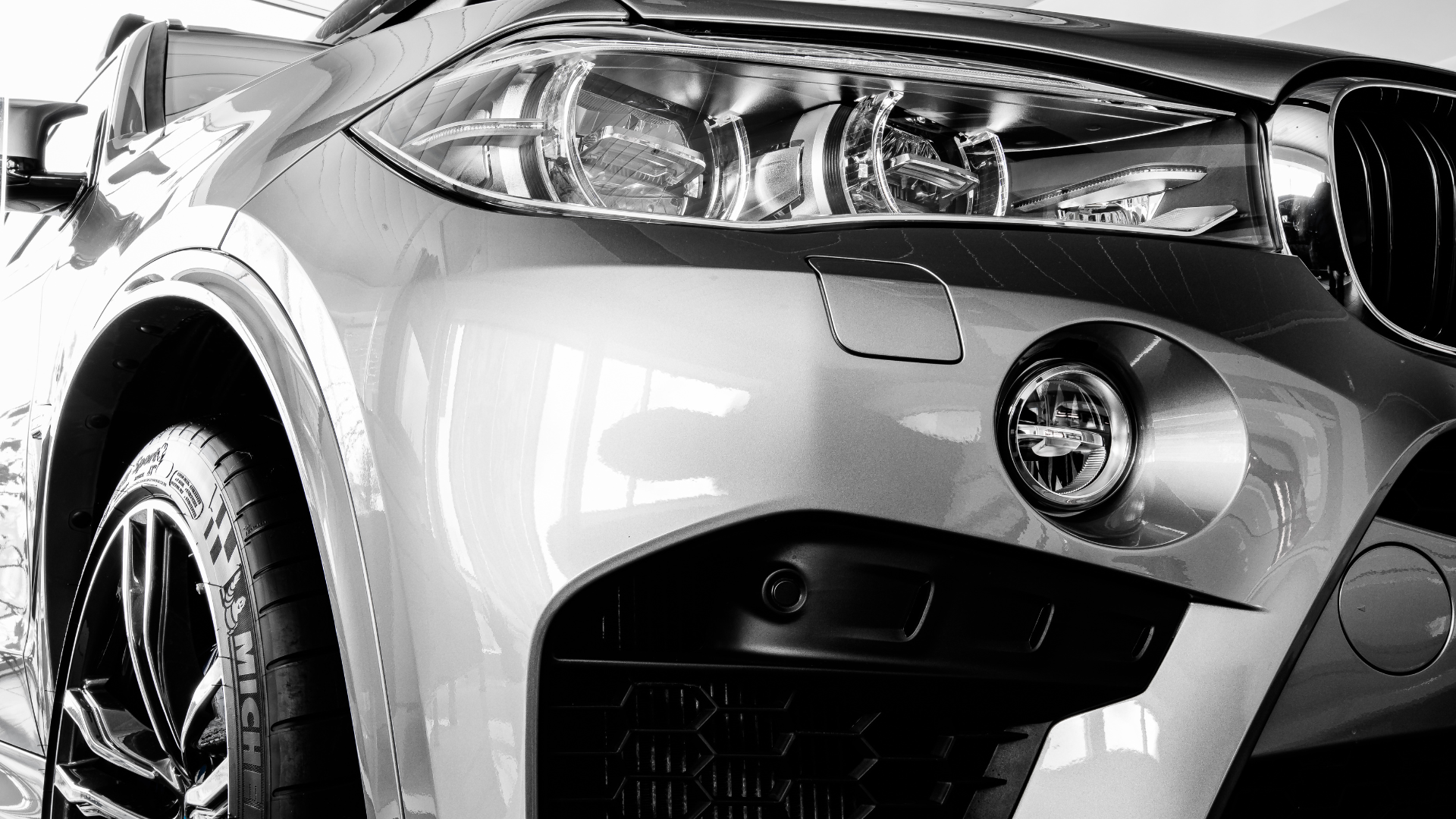 Close-up of the front of a silver SUV, showing the headlight, grille, and wheel in black and white.