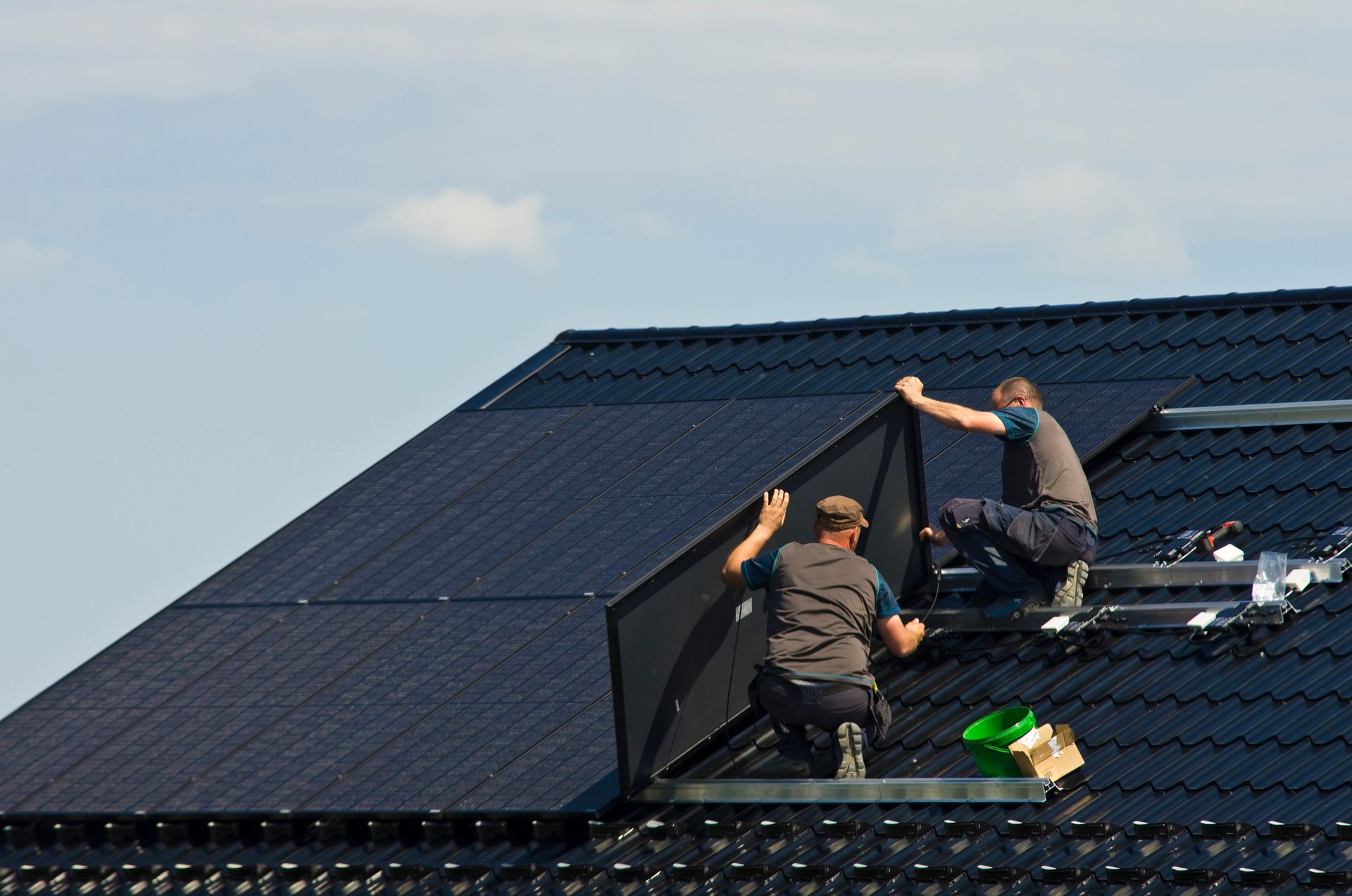 two men are installing solar panels on the roof of a house .