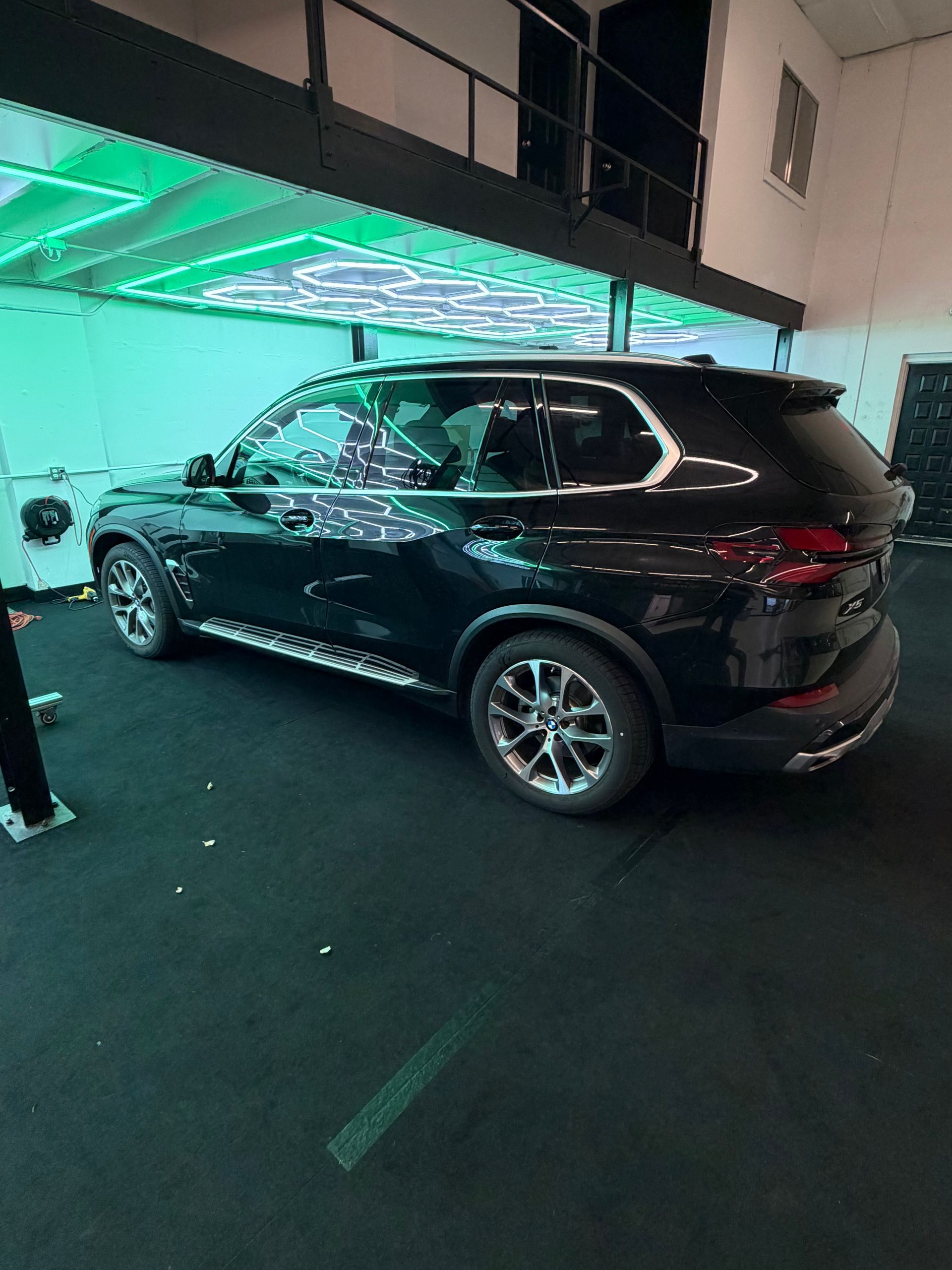 Black SUV parked under green-lit canopy at night, with a person standing nearby