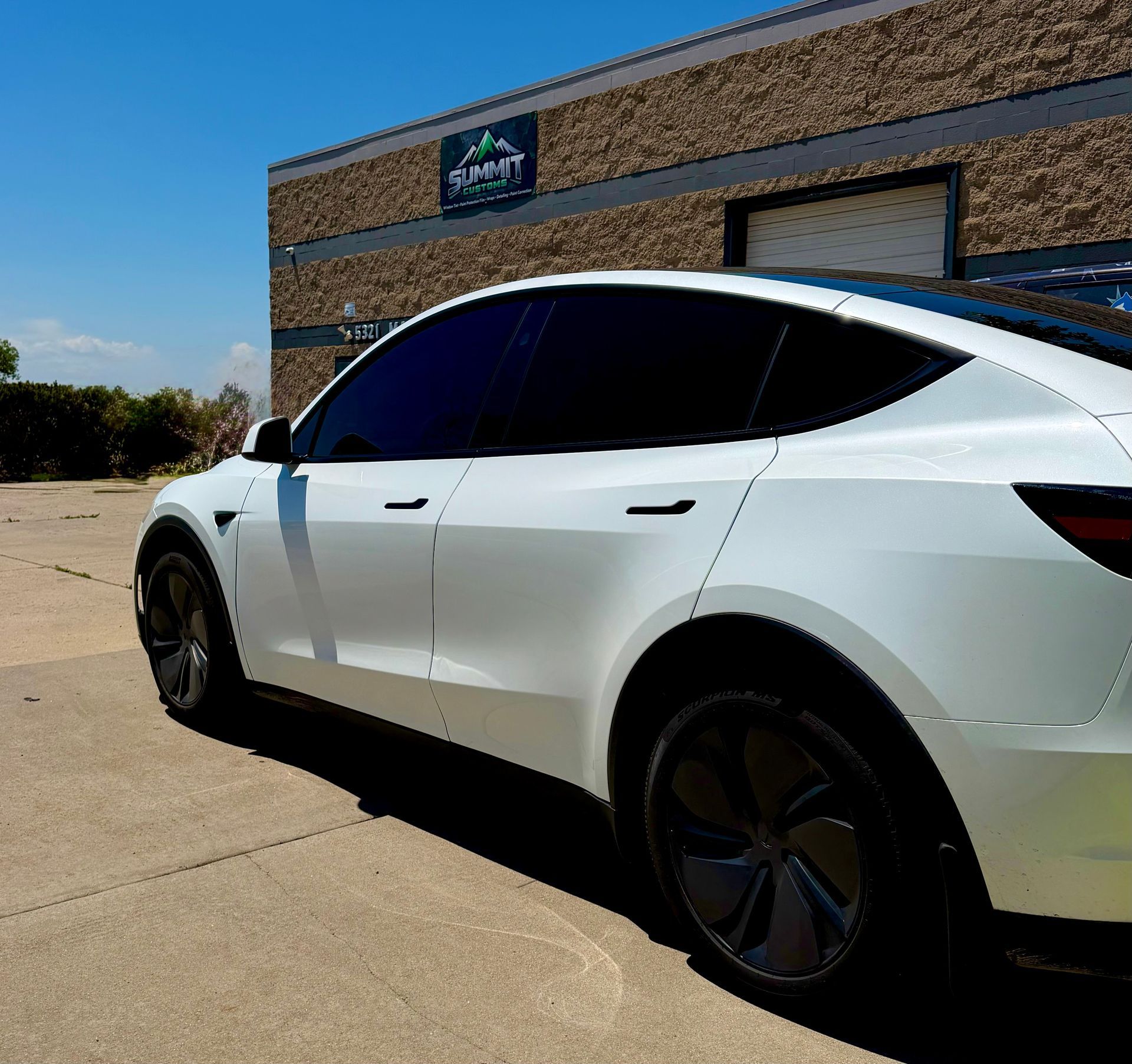 White Tesla parked beside Summit Customs building on a sunny day