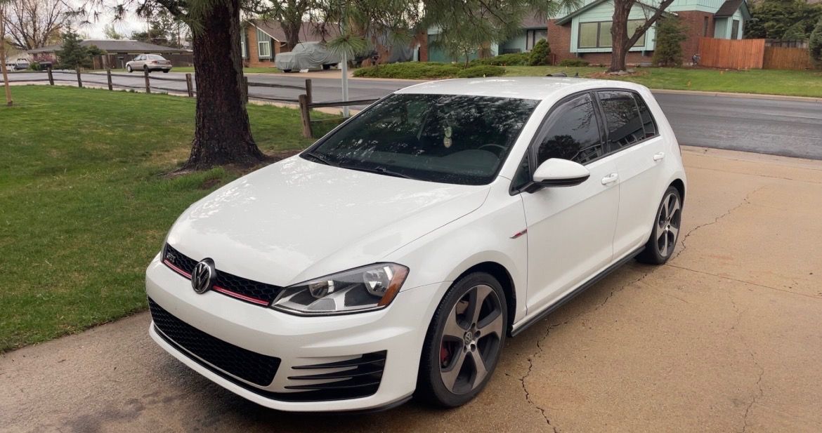 White hatchback parked on a suburban street beside a lawn and trees